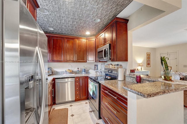 kitchen featuring light tile patterned floors, light stone countertops, kitchen peninsula, and appliances with stainless steel finishes