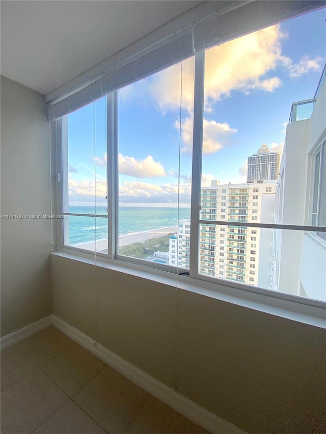 spare room with tile patterned flooring, a water view, and a view of the beach