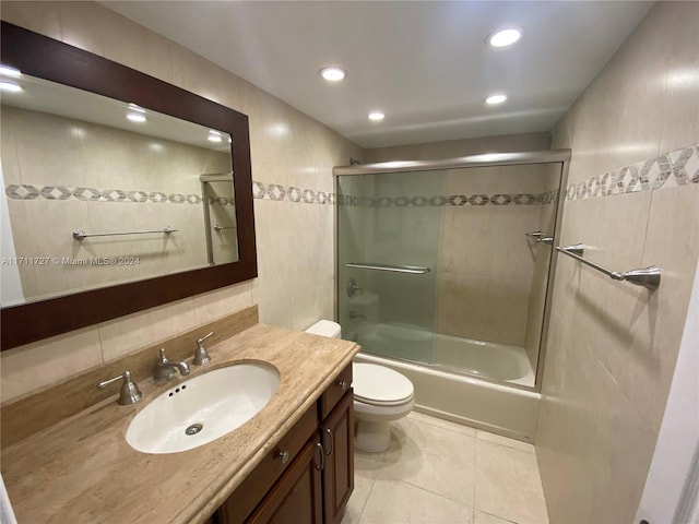 full bathroom with vanity, shower / bath combination with glass door, tile patterned flooring, toilet, and tile walls