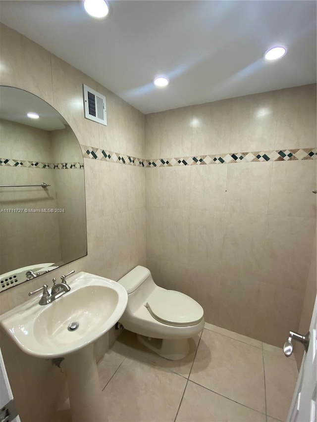 bathroom with toilet, tile patterned floors, and tile walls