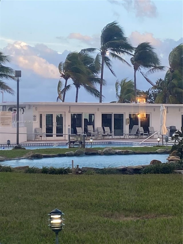 back house at dusk featuring a yard, a patio, and a swimming pool