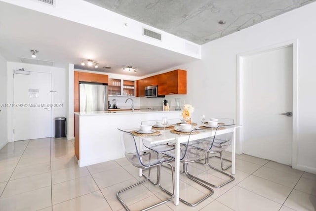 kitchen featuring kitchen peninsula, appliances with stainless steel finishes, a kitchen breakfast bar, sink, and light tile patterned floors