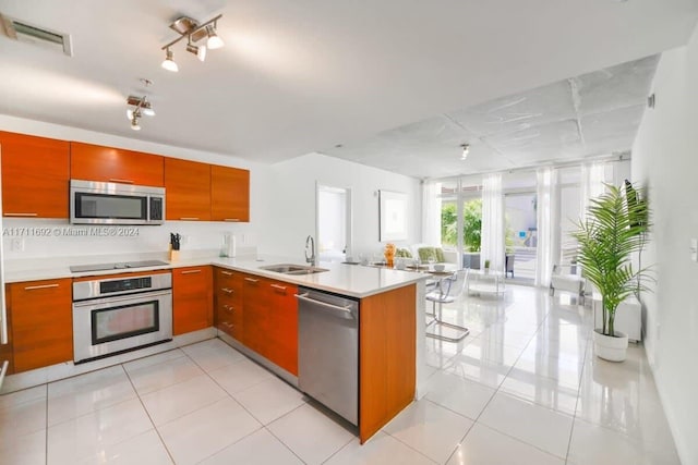 kitchen with light tile patterned flooring, kitchen peninsula, sink, and appliances with stainless steel finishes