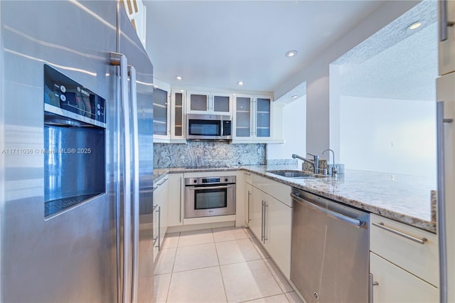 kitchen with light stone counters, light tile patterned floors, stainless steel appliances, glass insert cabinets, and a sink