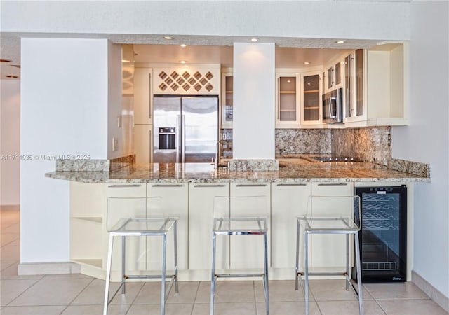 kitchen featuring white cabinets, wine cooler, glass insert cabinets, appliances with stainless steel finishes, and light stone countertops