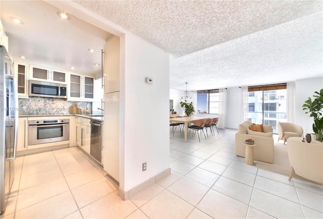 kitchen with light tile patterned floors, glass insert cabinets, open floor plan, stainless steel appliances, and backsplash