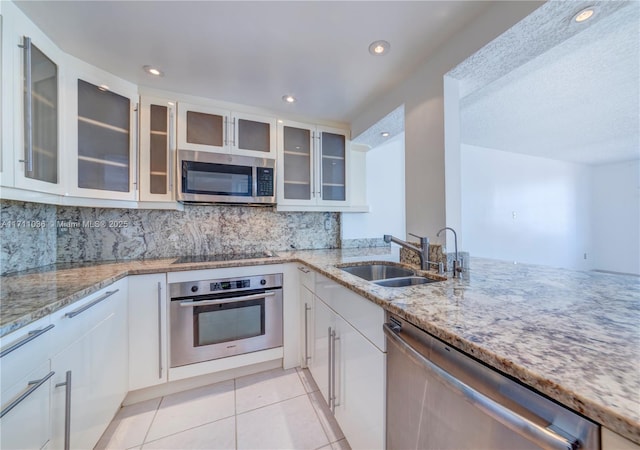 kitchen with light tile patterned floors, a sink, light stone countertops, appliances with stainless steel finishes, and white cabinetry
