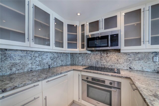 kitchen with decorative backsplash, light stone counters, stainless steel appliances, and white cabinetry