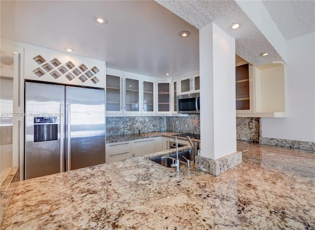 kitchen featuring stainless steel appliances, a sink, white cabinetry, glass insert cabinets, and light stone counters