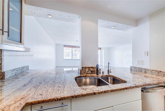 kitchen with a sink, a textured ceiling, glass insert cabinets, light stone countertops, and dishwasher