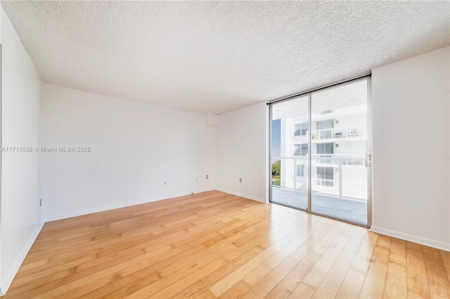 empty room featuring baseboards, a wall of windows, a textured ceiling, and light wood-style floors