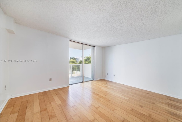 spare room with a textured ceiling, light wood-type flooring, baseboards, and floor to ceiling windows