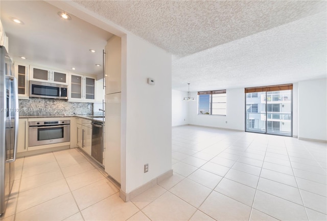 kitchen with light tile patterned floors, a textured ceiling, backsplash, and appliances with stainless steel finishes