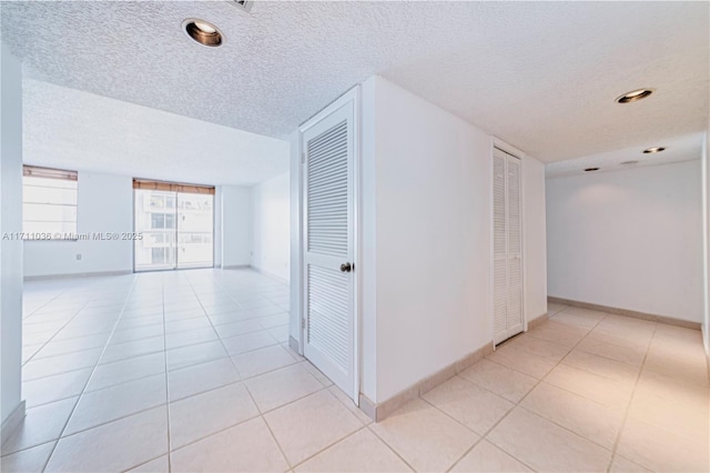 hall featuring recessed lighting, a textured ceiling, baseboards, and light tile patterned floors