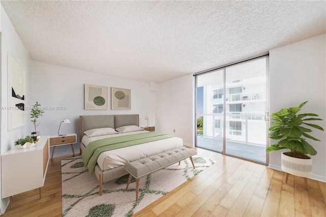 bedroom featuring access to outside, floor to ceiling windows, a textured ceiling, and light wood-style flooring