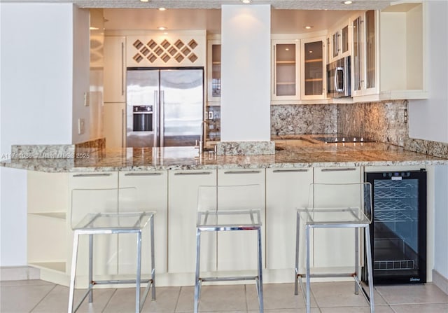 kitchen with wine cooler, glass insert cabinets, appliances with stainless steel finishes, white cabinets, and light stone countertops