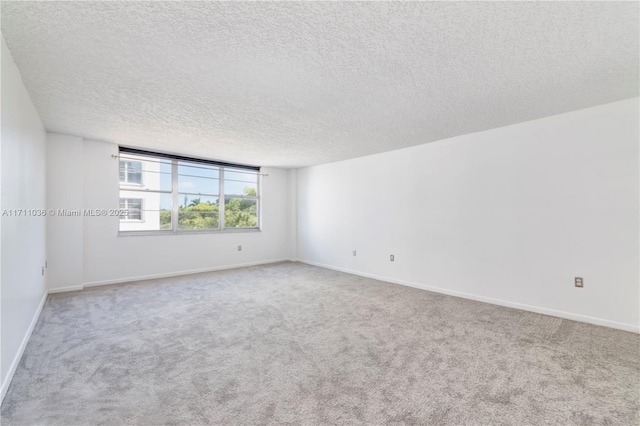 carpeted spare room with a textured ceiling and baseboards