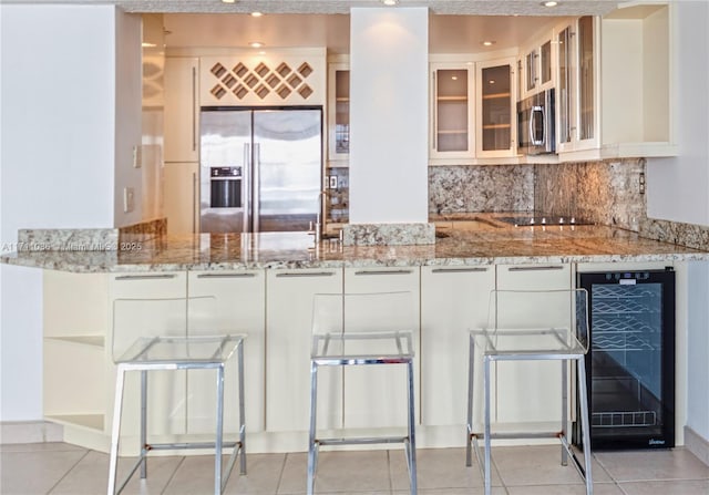 kitchen featuring a peninsula, beverage cooler, stainless steel appliances, and light stone countertops