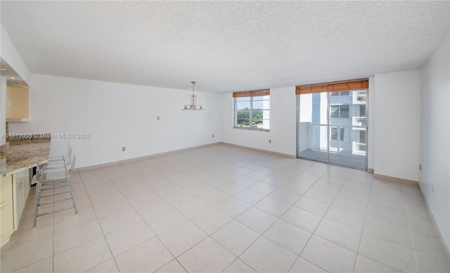 unfurnished living room featuring baseboards, a notable chandelier, a textured ceiling, and light tile patterned floors