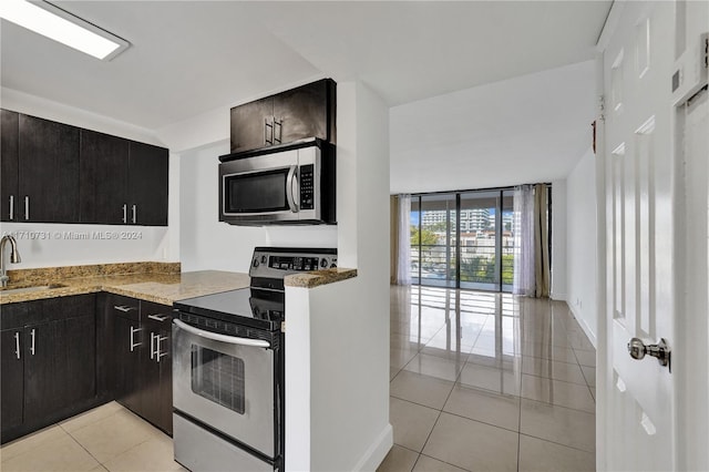 kitchen with expansive windows, sink, light tile patterned floors, light stone counters, and stainless steel appliances