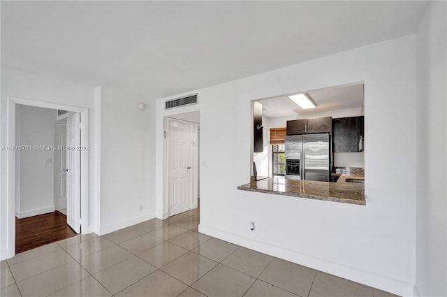 kitchen featuring stone counters, kitchen peninsula, light tile patterned floors, dark brown cabinets, and stainless steel fridge with ice dispenser