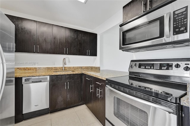 kitchen with sink, light stone countertops, light tile patterned floors, dark brown cabinetry, and stainless steel appliances