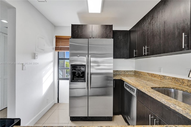 kitchen featuring dark brown cabinetry, light tile patterned floors, stone countertops, and appliances with stainless steel finishes