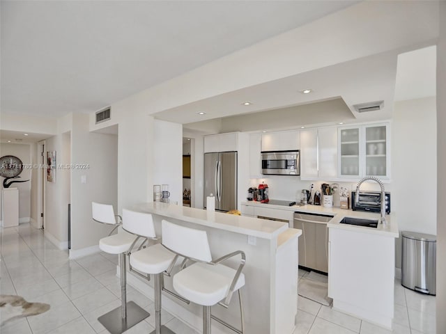 kitchen with kitchen peninsula, appliances with stainless steel finishes, light tile patterned floors, white cabinets, and a breakfast bar area