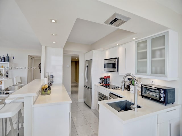 kitchen with white cabinets, sink, light tile patterned floors, kitchen peninsula, and stainless steel appliances