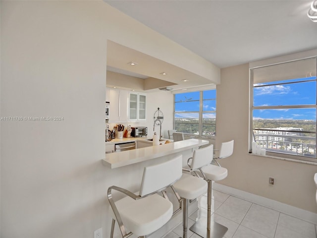 interior space featuring white cabinetry, stainless steel appliances, kitchen peninsula, a kitchen bar, and light tile patterned floors