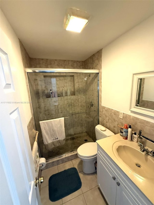 bathroom featuring tile patterned floors, toilet, a shower with door, vanity, and tile walls