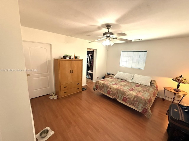 bedroom with a spacious closet, ceiling fan, wood-type flooring, and a closet