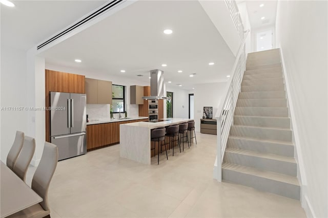 kitchen featuring a center island, tasteful backsplash, island range hood, a kitchen bar, and stainless steel appliances