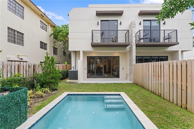 back of property featuring a fenced in pool, central air condition unit, a balcony, and a lawn