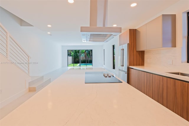 kitchen with exhaust hood, black electric stovetop, sink, decorative backsplash, and high quality fridge