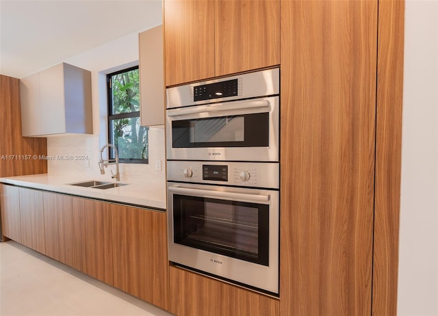 kitchen with backsplash, stainless steel double oven, and sink