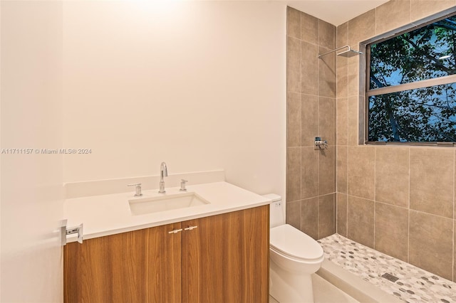 bathroom featuring a tile shower, vanity, and toilet