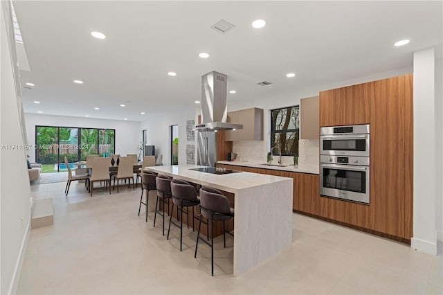 kitchen featuring a center island, a kitchen breakfast bar, sink, stainless steel double oven, and island exhaust hood