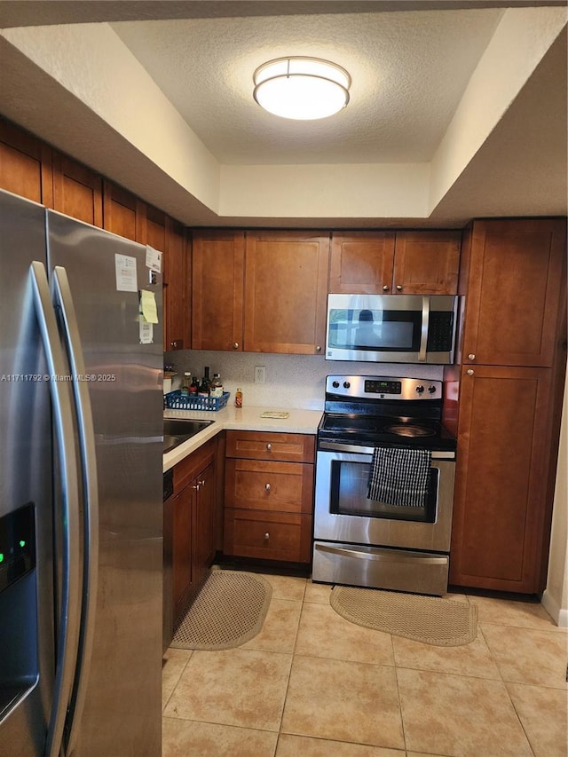 kitchen with sink, a textured ceiling, stainless steel appliances, and light tile patterned flooring