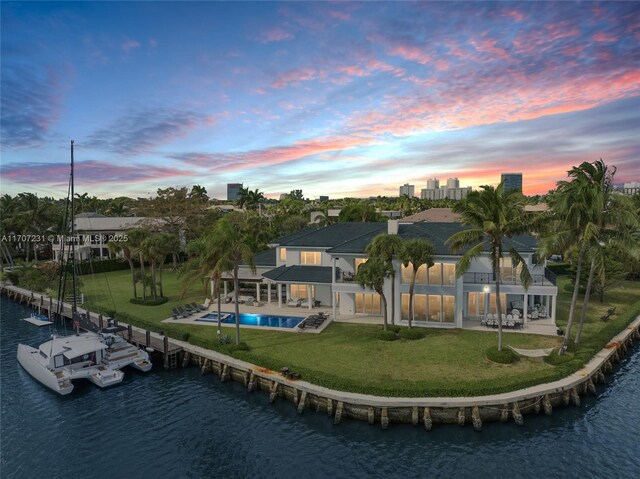 pool at dusk featuring an in ground hot tub, ceiling fan, a water view, and a patio