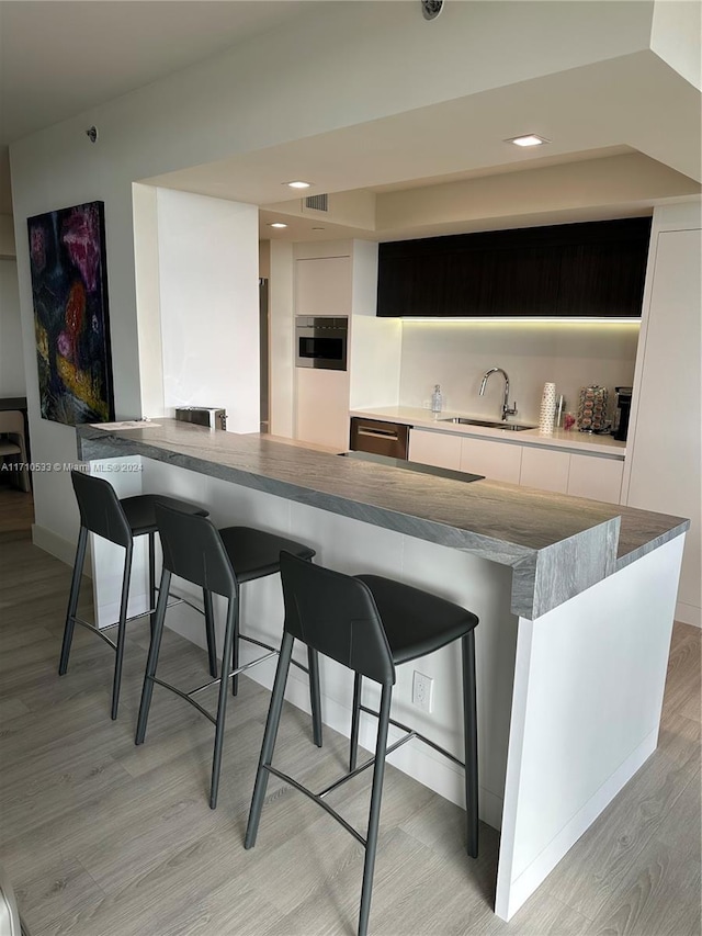 bar featuring stainless steel appliances, sink, light hardwood / wood-style floors, and dark brown cabinets