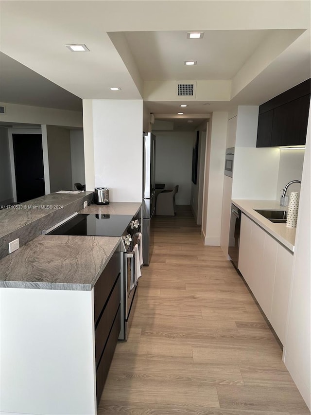 kitchen featuring sink, stainless steel appliances, kitchen peninsula, white cabinets, and light wood-type flooring