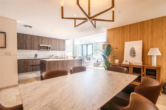 kitchen featuring sink, a kitchen breakfast bar, wood walls, a chandelier, and a kitchen island with sink