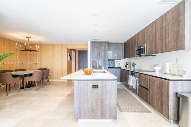 kitchen with sink, an inviting chandelier, pendant lighting, a kitchen island with sink, and appliances with stainless steel finishes