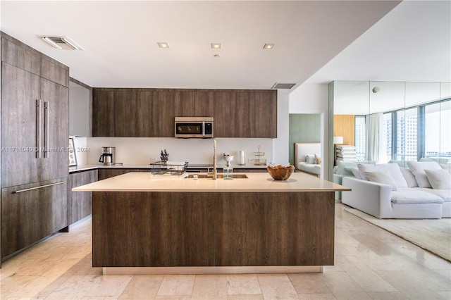 kitchen featuring paneled fridge, dark brown cabinets, a center island with sink, and sink