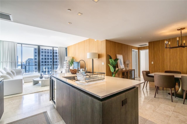 kitchen featuring sink, decorative light fixtures, wood walls, a chandelier, and an island with sink