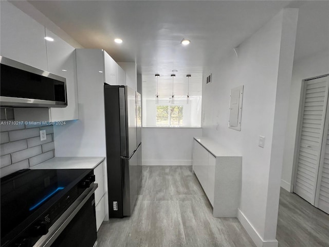 kitchen with white cabinetry, light wood-type flooring, decorative light fixtures, and appliances with stainless steel finishes