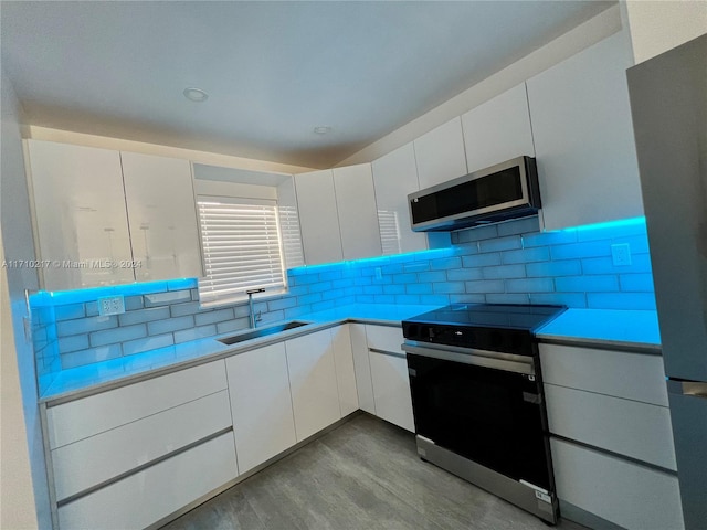 kitchen featuring white cabinetry, sink, stainless steel appliances, tasteful backsplash, and light wood-type flooring