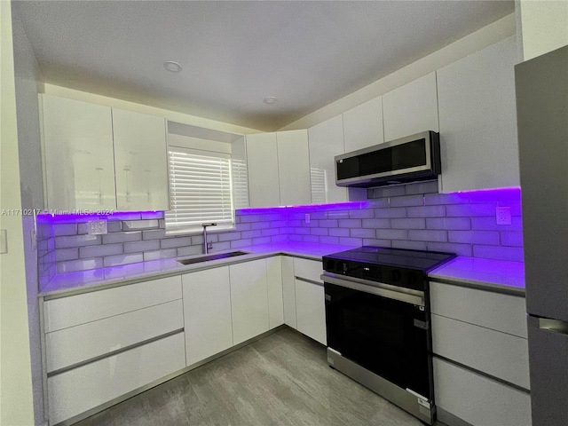 kitchen with white cabinetry, sink, stainless steel appliances, and light hardwood / wood-style flooring