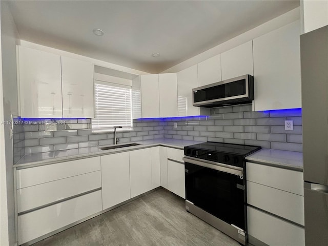 kitchen with appliances with stainless steel finishes, light wood-type flooring, backsplash, sink, and white cabinets